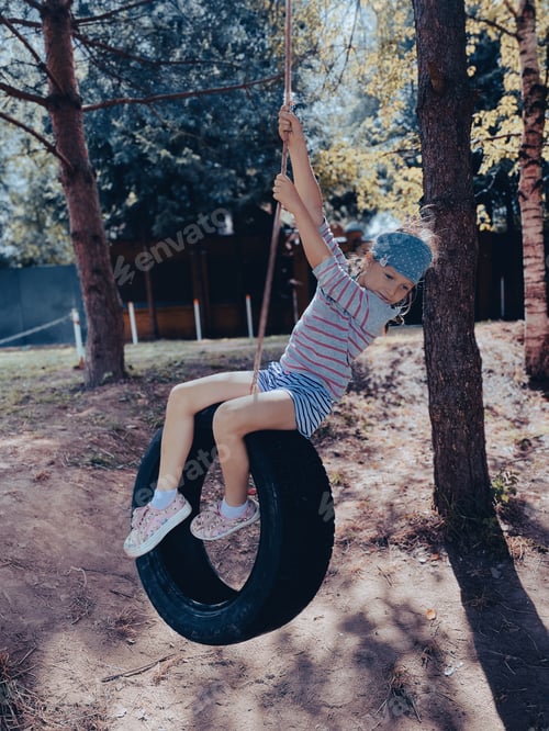 Preview: A girl in the suburbs rides a tire tied to a tree.