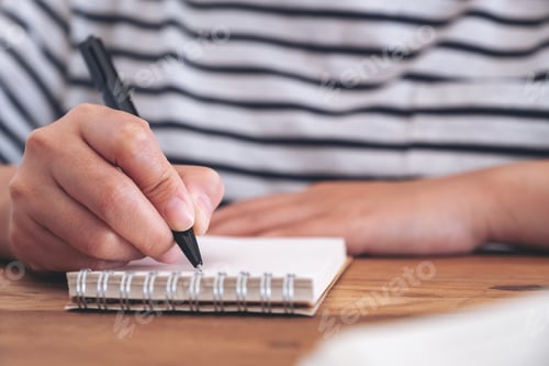 Preview: Closeup image of a woman's hand writing on blank notebook on wooden table