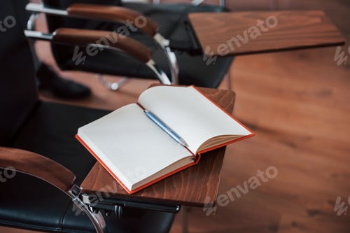 Preview: Notepad with red cover lying on the stand of chair in the business classroom