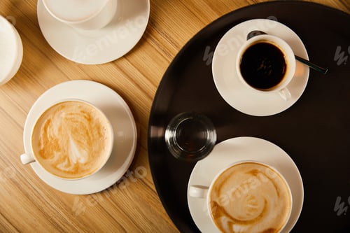 Preview: top view of cups of different coffee near glass of water on tray