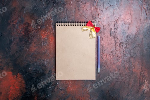 Preview: top view a notepad with little bow pen on dark red ground copy place