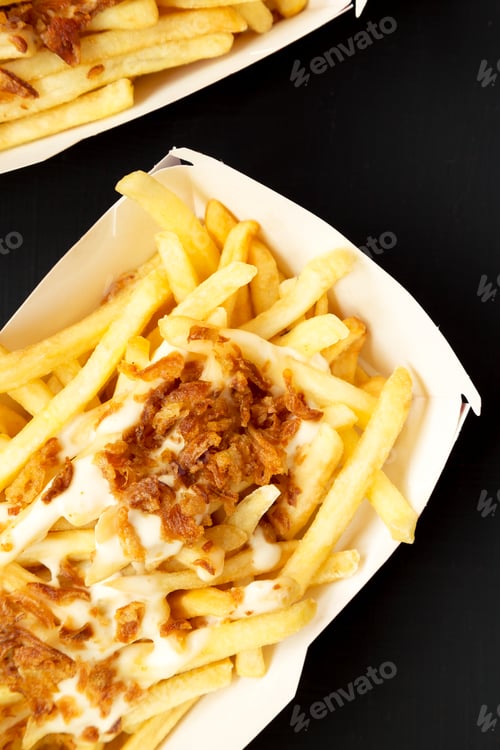 Preview: French fries with cheese sauce and fried onion in paper boxes on a black surface, top view.