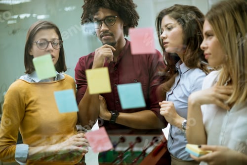 Preview: Young business people discussing in front of glass wall using post it notes and stickers