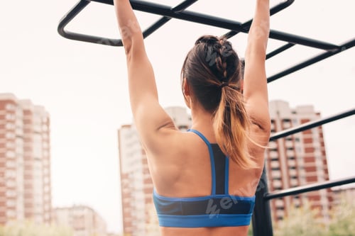 Preview: Attractive fit young woman in sport wear girl pulls up on the bar at street workout area