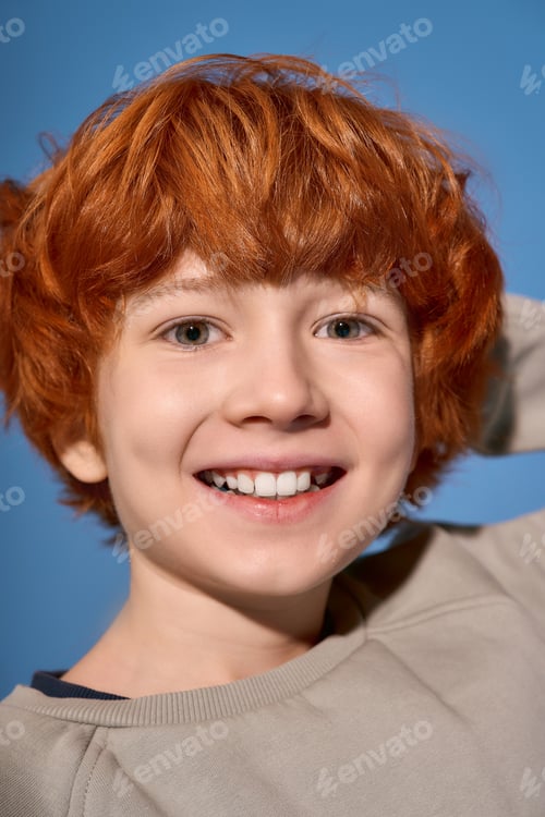 Preview: Little stylish boy with bright red hair smiles joyfully against a vibrant blue background