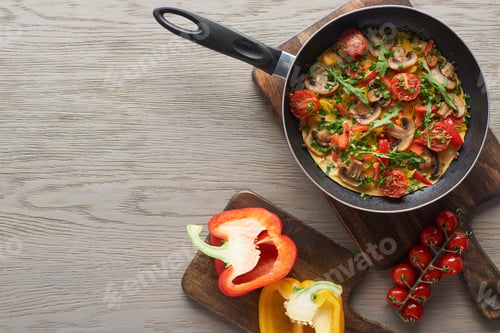 Preview: top view of homemade omelet in frying pan on wooden board with bell peppers and cherry tomatoes