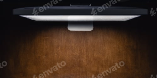 Preview: Computer monitor on a wooden table in a dark room, top view.