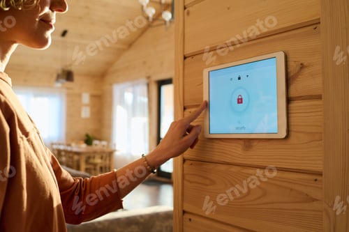 Preview: Hand of young woman on panel of alarm system with lock sign on screen