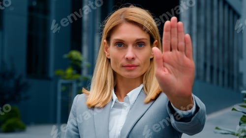 Preview: Serious woman standing outdoors looking at camera showing stop gesture holding palm in front