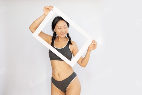 Preview: Asian girl holding frame posing in lingerie and having fun. Concept about body positivity