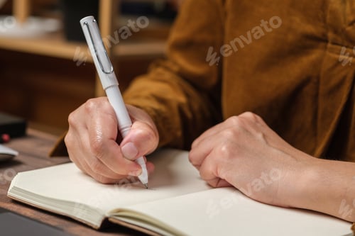 Preview: close uop woman hand writing on notebook at worknig desk at home