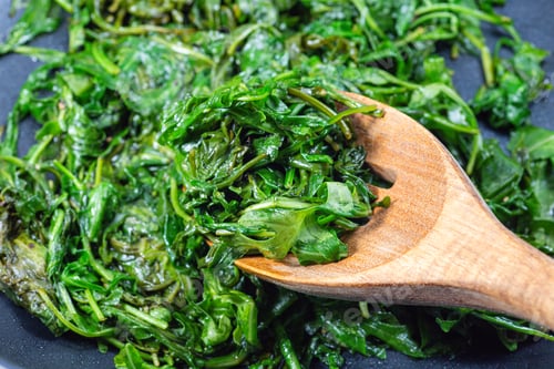 Preview: Wilted arugula or rocket salad, preparing a side dish in frying pan, horizontal closeup