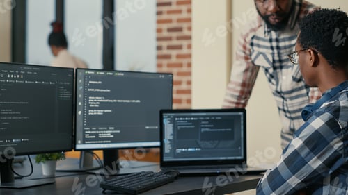 Preview: Focused software developer writing code on laptop looking at multiple screens with programming