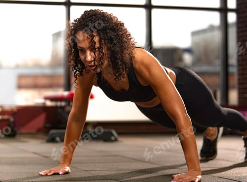 Preview: African American sportswoman train in the gym doing push-ups from the floor. Attractive female