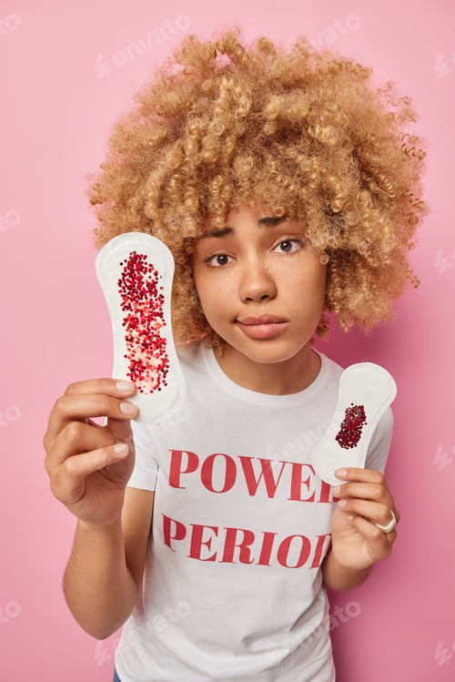 Preview: Serious young woman holds two types of sanitary napkins smeared with red glitters as if blood tells