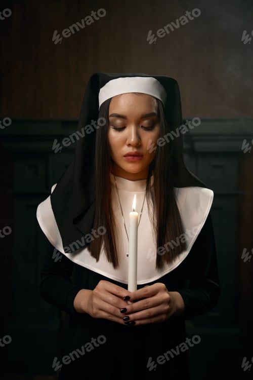 Preview: Portrait of beautiful nun in monastic robe holding burning candle in hands
