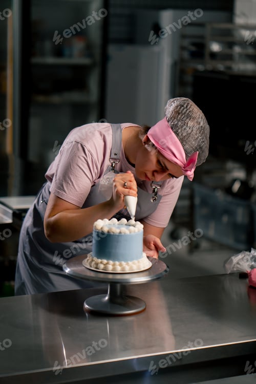 Preview: of a female baker in a professional kitchen decorating a blue cake with cream