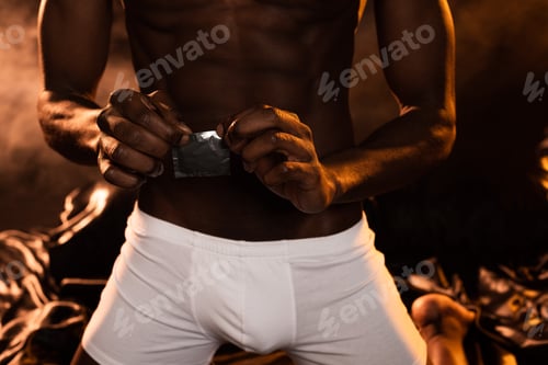 Preview: cropped view of african american man in white boxers holding condom on bed