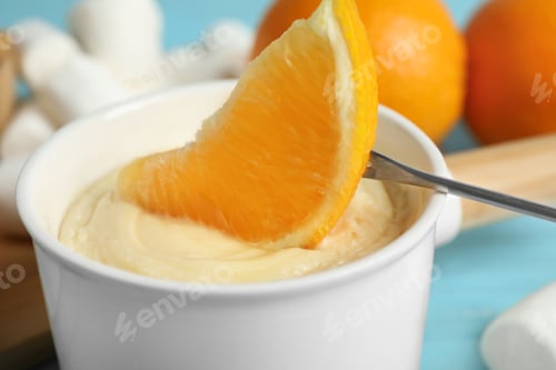 Preview: Dipping slice of orange into pot with white chocolate fondue, closeup