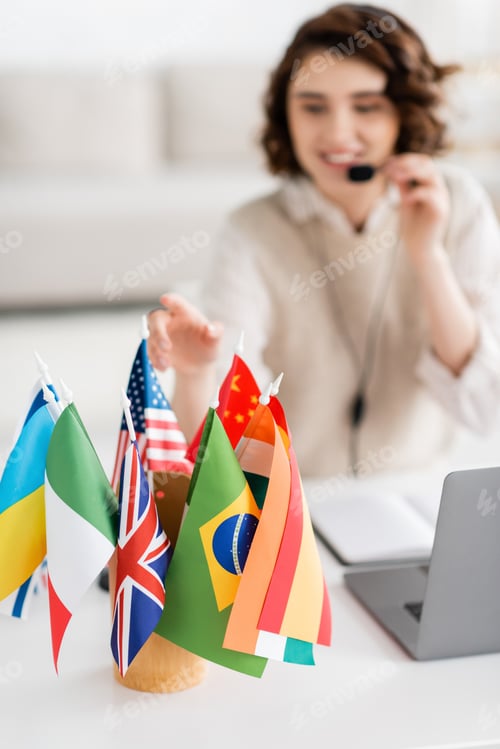 Preview: selective focus of various international flags near laptop and blurred language teacher working at