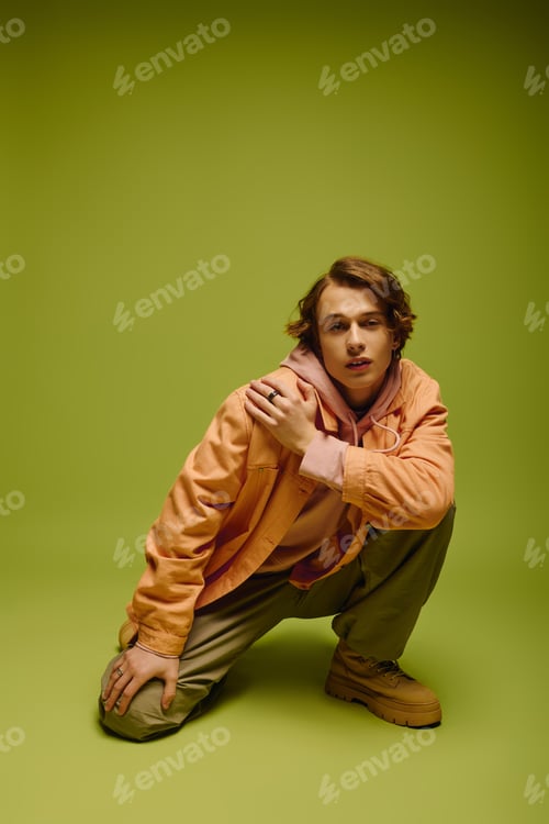 Preview: Young man showcasing modern fashion trends against a vibrant green backdrop in a stylish pose
