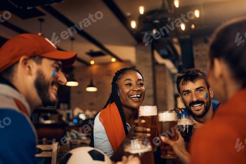 Preview: Young happy soccer fans toasting with beer in pub.