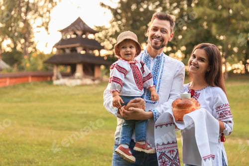 Preview: Happy cute family in embroidered Ukrainian shirts with korovai bread on sunny day. Space for text