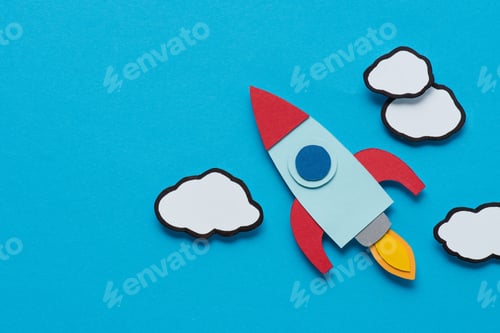 Preview: top view of cardboard rocket with clouds on blue background, setting goals concept