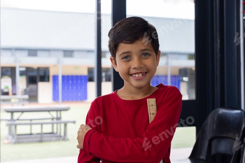Preview: Biracial boy with a bright smile, wearing a red shirt, stands confidently at school