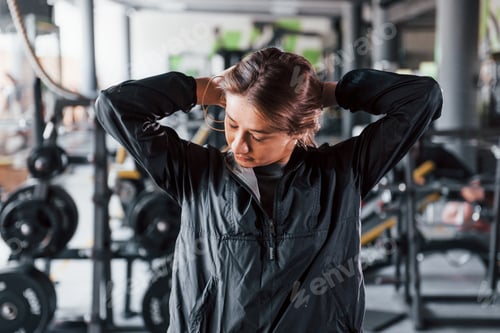 Preview: Young girl in black sportwear preparing for exercises in modern gym
