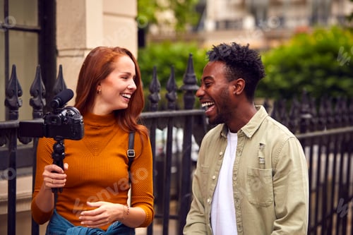 Preview: Young Couple Travelling Through City Together Vlogging To Video Camera On Handheld Tripod