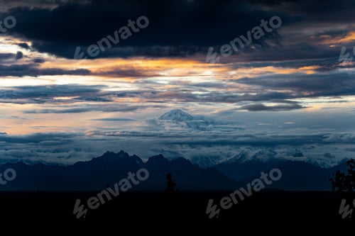 Preview: Aerial view of snowy Denali mountain at a distance under dark colorful sunset sky in Alaska