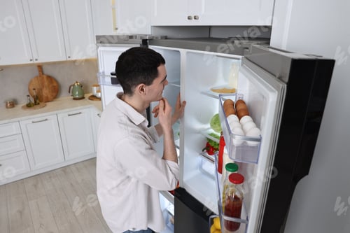 Preview: Thoughtful man near refrigerator in kitchen at home