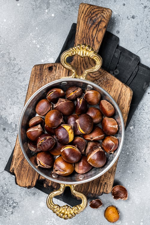 Preview: Cracked roasted chestnuts served in a skillet. Gray background. Top view