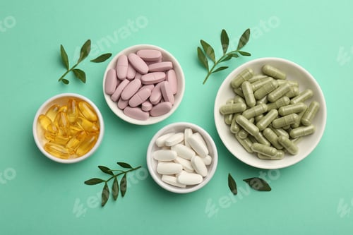 Preview: Different vitamin capsules in bowls and leaves on turquoise background, flat lay