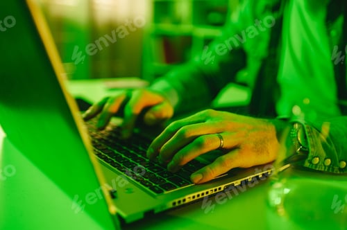 Preview: Close-up of a website designer sitting at a green-lighted home office and typing code on a laptop.