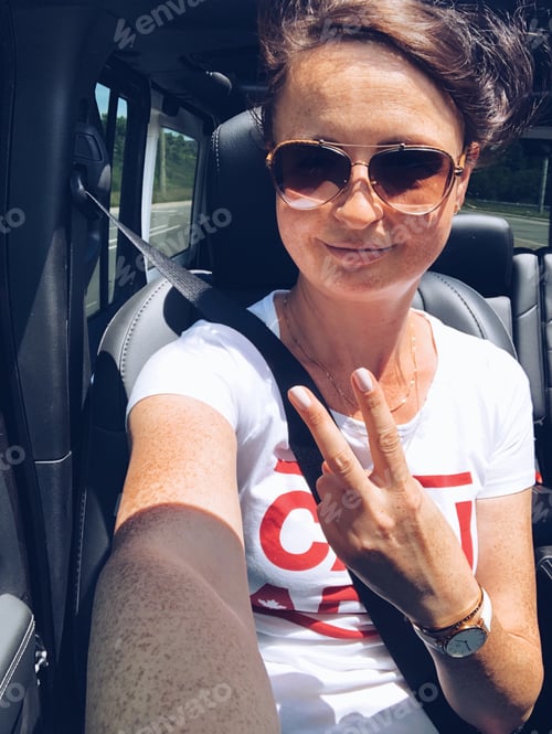Preview: A happy selfie of a smiling woman riding in a car with the sunroof open and wind blowing her hair