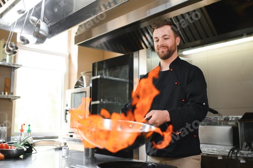Preview: Chef in restaurant kitchen at stove and pan cooking flambe on food
