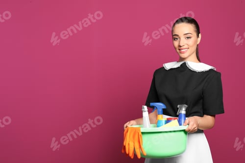 Preview: Young chambermaid holding plastic basin with detergents on color background