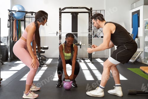 Preview: Fitness people cheering and supporting woman while exercising with a kettlebell at the gym.