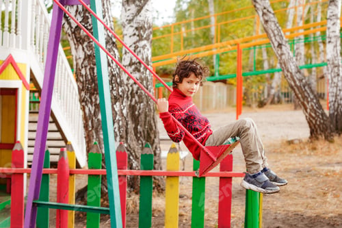 Preview: Curly Asian boy swinging on swing in autumn kids playground