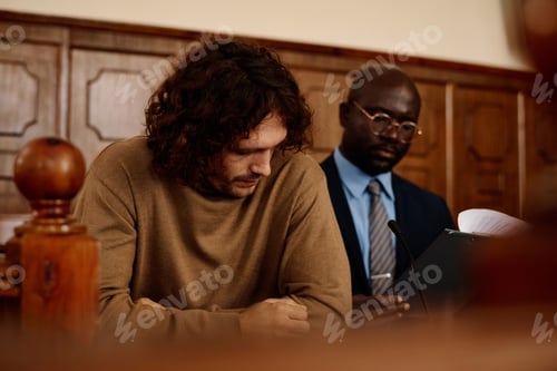 Preview: Focus on young male suspect sitting by desk in front of camera