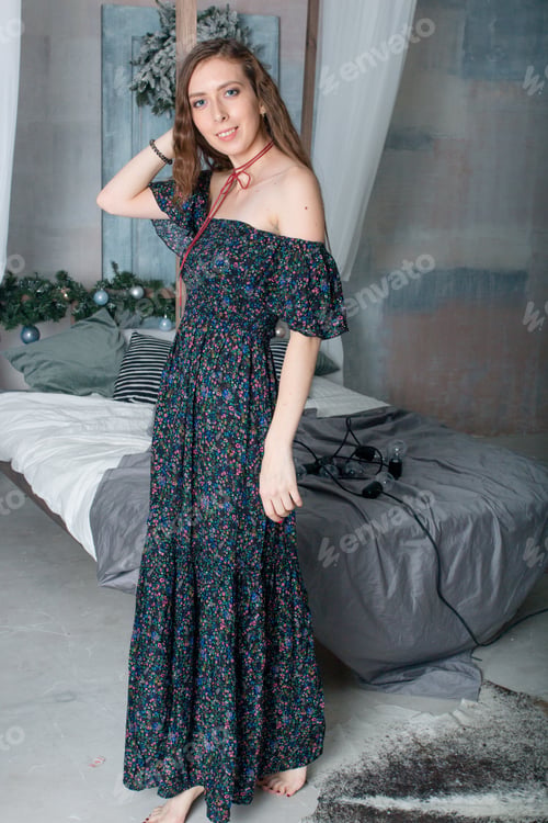 Preview: a girl with long dark hair, in a long dress with bare shoulders, in her bedroom.