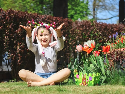 Preview: Little caucasian girl with a happy smile and a headband with bunny ears throws chocolate Easter eggs