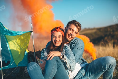 Preview: Young happy couple holding smoke bombs on camping