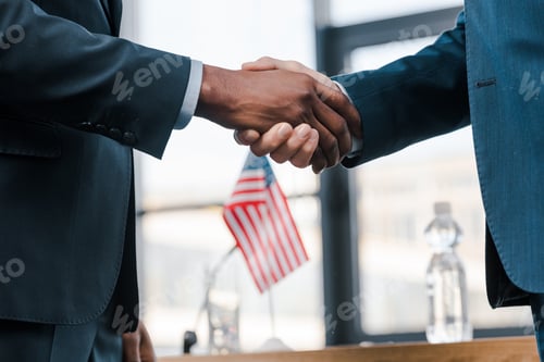 Preview: cropped view of multicultural diplomats shaking hands near flag of america