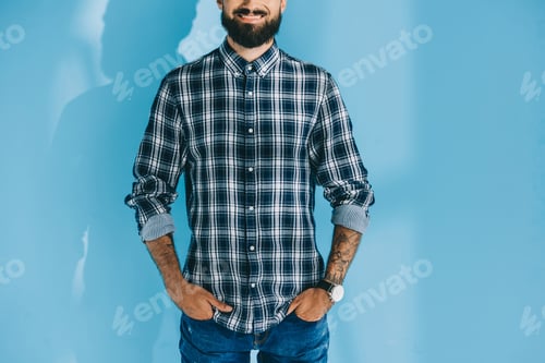 Preview: cropped view of bearded man standing with hands in pockets, on blue