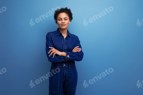 Preview: portrait of a young woman with dark skin and black curly hair dressed in blue denim overalls