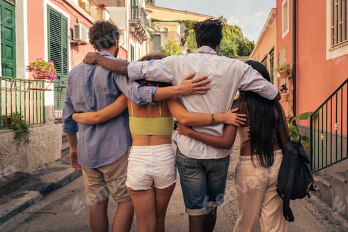 Preview: Multicultural group of young friends walking arm in arm through sunny Mediterranean street