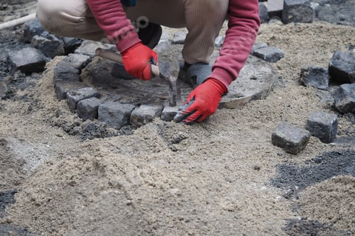 Preview: Worker adds stones to a circular area on a construction site